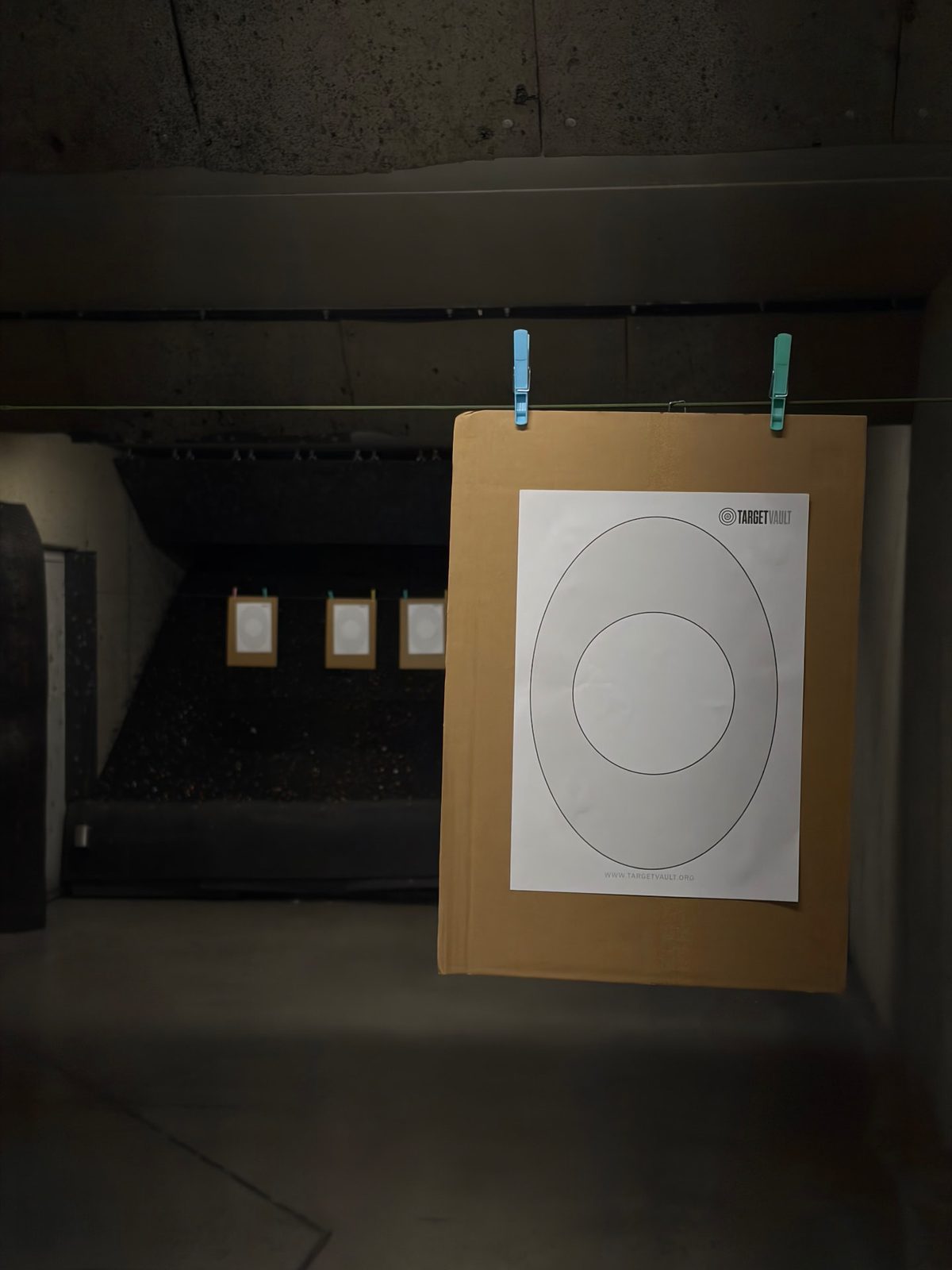A printed TargetVault A4 target clipped to cardboard on the line of an indoor shooting range